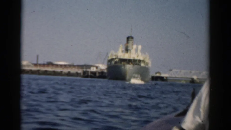 Large mid-century cargo or passenger ship docked at a pier, filmed from a small boat on choppy water, circa 1957, Catskill New York area.