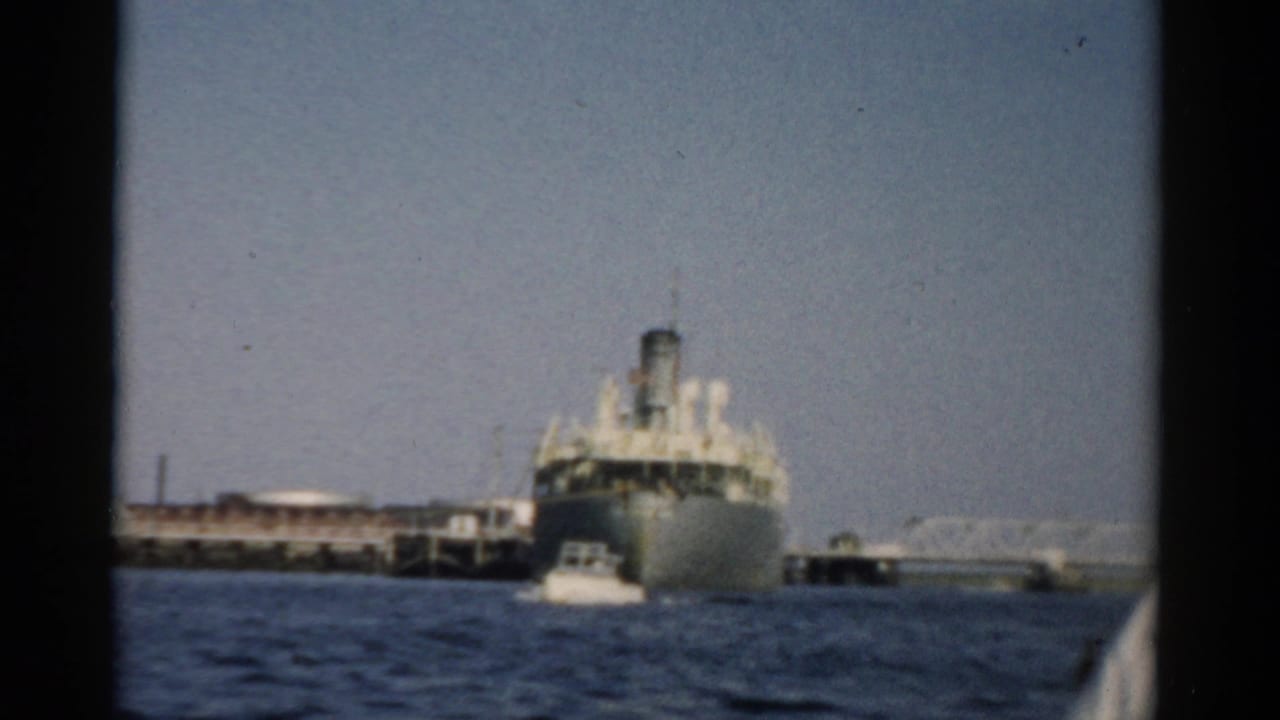 Mid-century passenger or cargo ship moored at a port, filmed from a small boat with a motorboat visible alongside, circa 1957 Catskill New York.