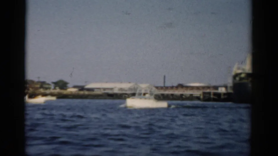 Small motorboat on choppy water with an ocean-going vessel and industrial pier in background, circa 1957 home movie, Catskill New York area.