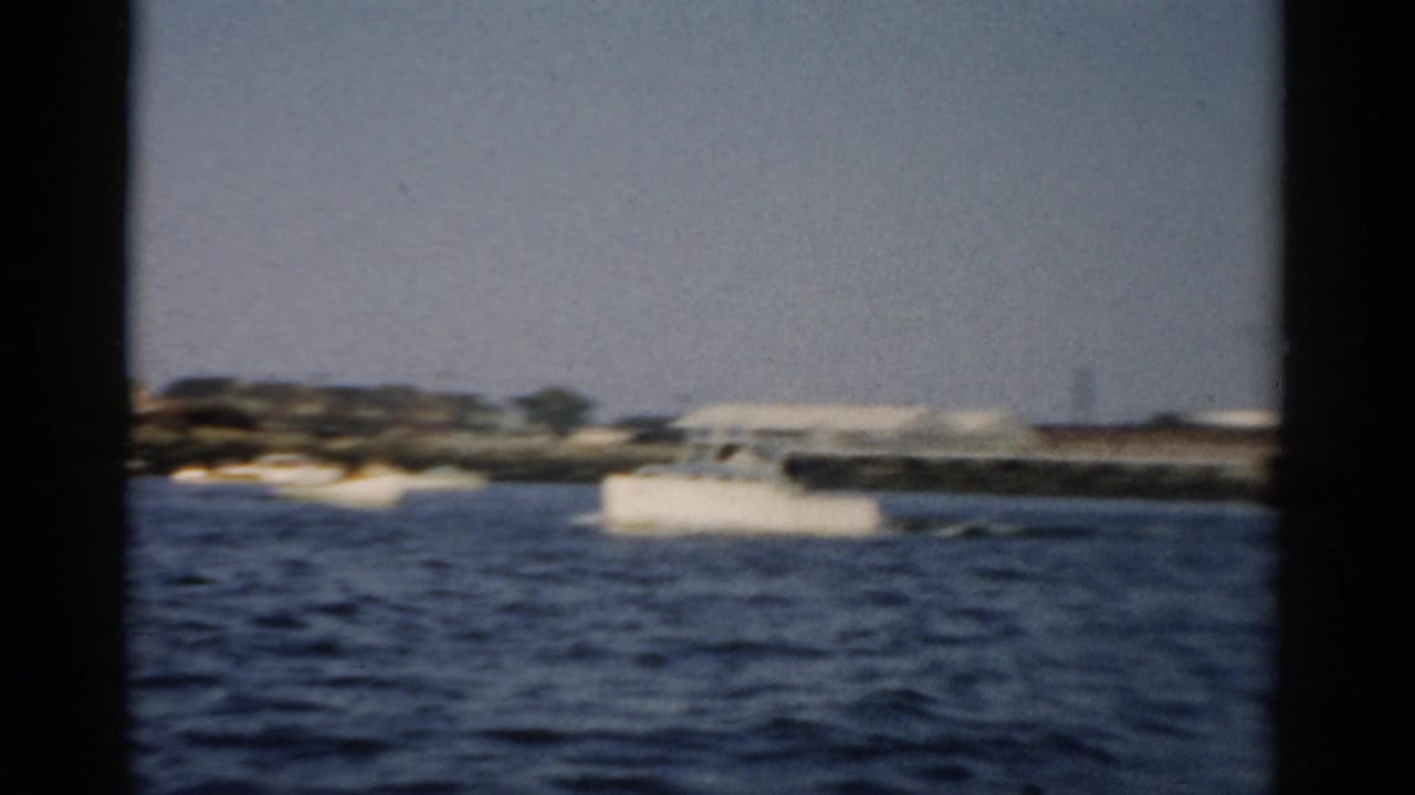 Waterfront view on 8mm circa 1957, showing dark rippled water, a distant low shoreline with buildings, and a pale gray-blue sky consistent with the Catskill, New York area.