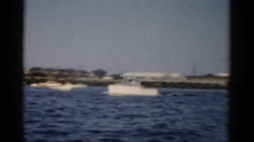 Waterfront view on 8mm circa 1957, showing dark rippled water, a distant low shoreline with buildings, and a pale gray-blue sky consistent with the Catskill, New York area.