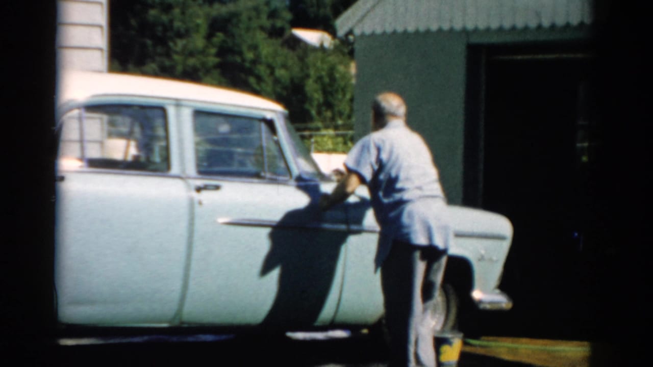 Man in blue shirt hand-drying the side of a pale blue late-1950s sedan beside a corrugated metal garage, Catskill NY area, 1957.