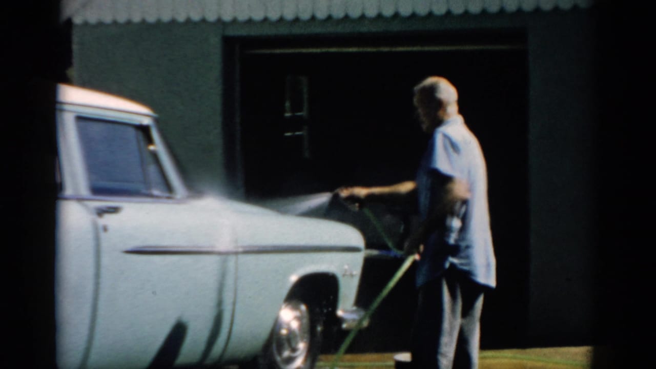 Man hosing down a pale blue mid-1950s American sedan in front of a corrugated-roof garage, Catskill, New York, circa 1957.