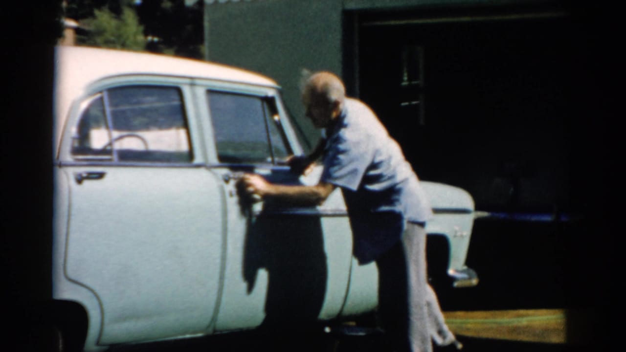 Man cleaning the side door of a pale blue mid-1950s American sedan with a cloth, circa 1957, Catskill, New York.