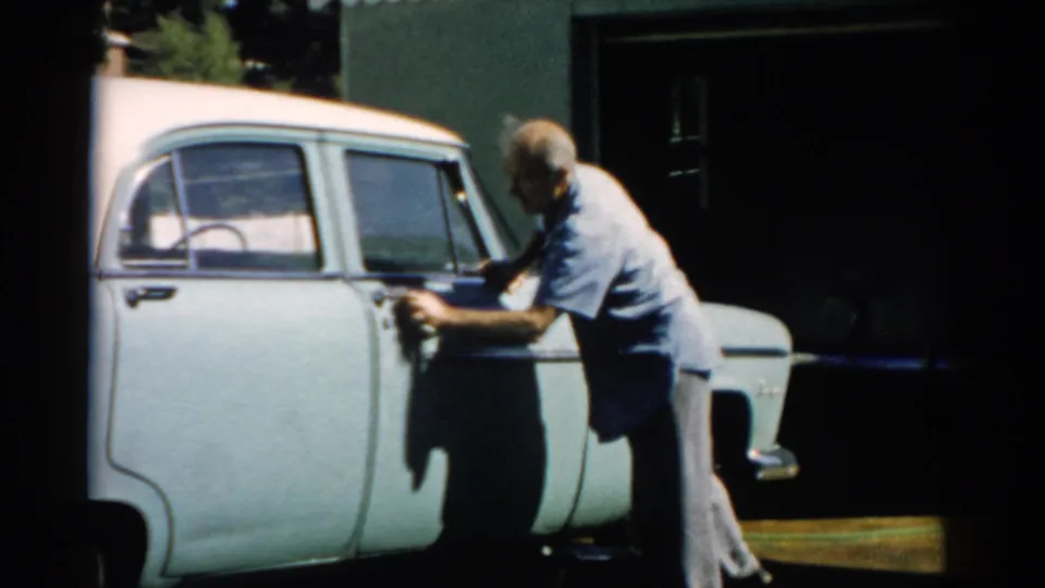 Man cleaning the side door of a pale blue mid-1950s American sedan with a cloth, circa 1957, Catskill, New York.