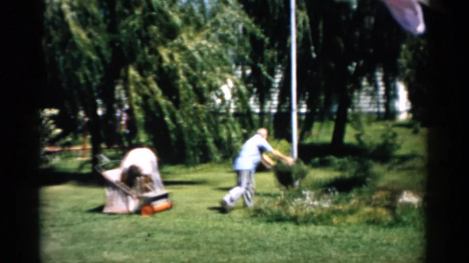Couple working with a reel mower and grass-catcher bag in a suburban yard, Catskill, New York, circa 1957.