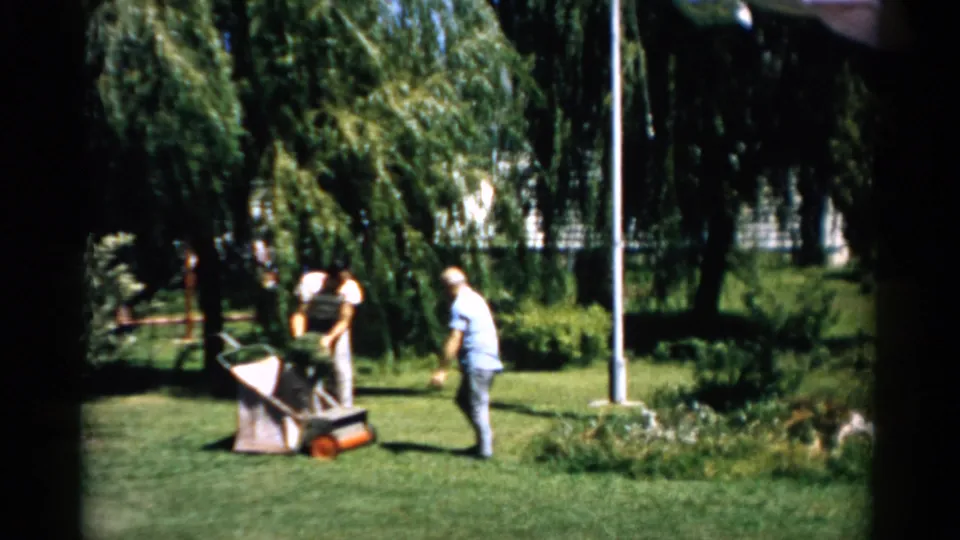 Man and woman adjusting a reel mower grass-catcher bag in a residential garden, Catskill, New York, circa 1957.