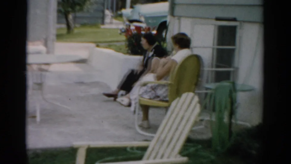 Two women seated in striped metal chairs on a patio in Catskill, New York, circa 1957; the rear of a late-1950s automobile is visible at upper right.