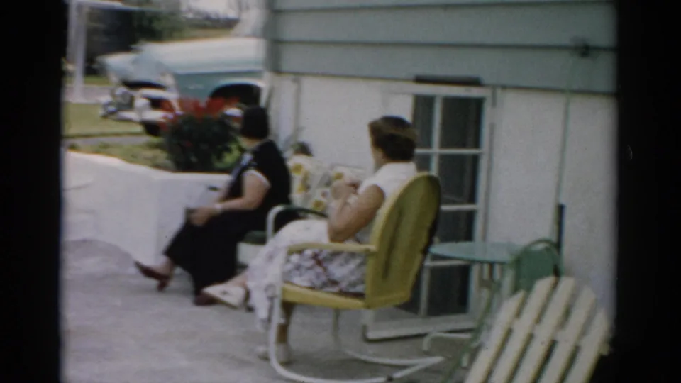 Candid 8mm shot of two women in conversation outside a residential home, circa 1957, Catskill, New York area.