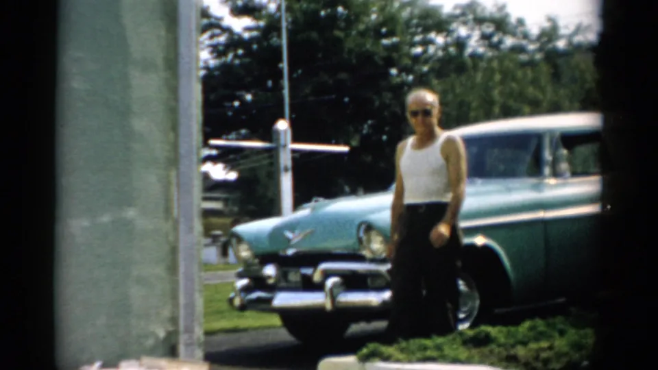 Man in sunglasses posing before a two-tone teal 1950s American sedan, Catskill, New York area, circa 1957.