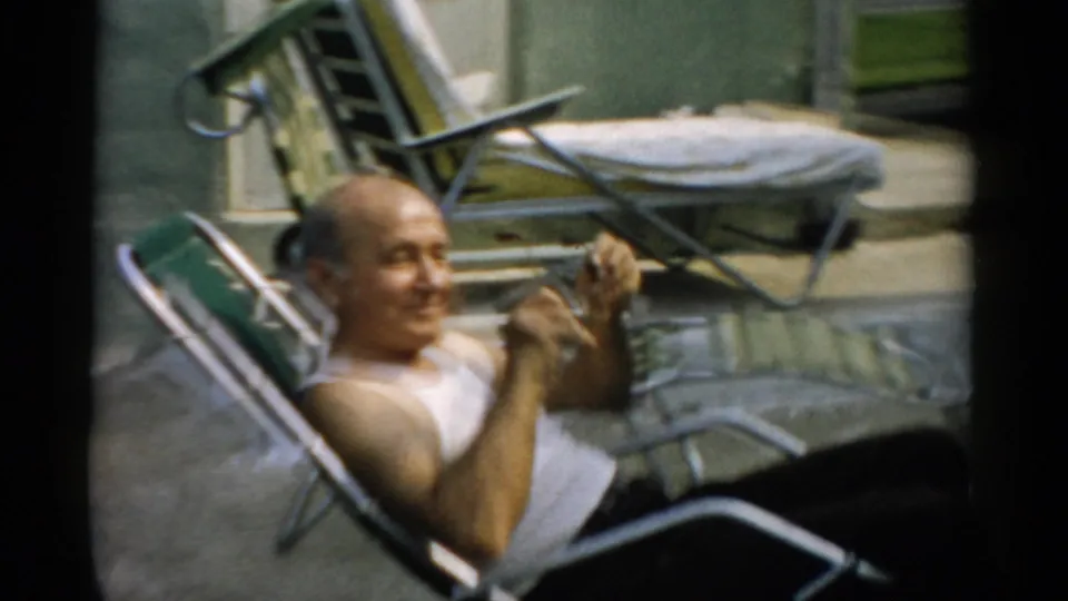 Elderly man reclines in aluminum chaise lounge, smiling and touching his face, additional lawn chairs in background, Catskill, New York, ca. 1957.