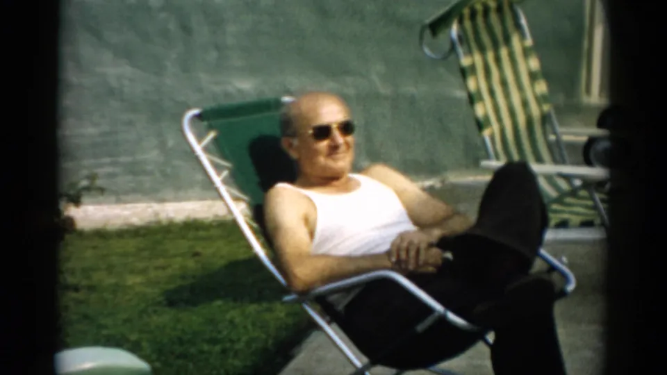 Bald man smiling in a green metal reclining chair outdoors, 8mm home movie footage, circa 1957, Catskill, New York.