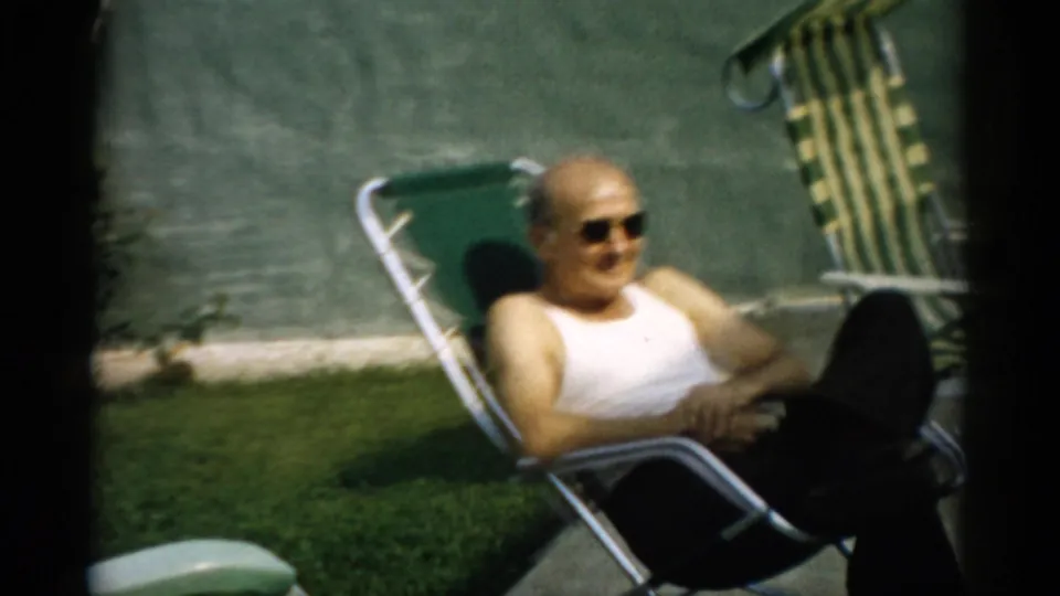 Bald man at ease in a green metal reclining lawn chair, 8mm home movie, circa 1957, Catskill, New York region.