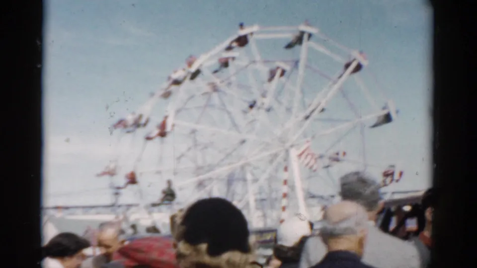 Large white Ferris wheel with red gondolas above a crowd at what appears to be a 1950s upstate New York county fair, filmed on 8mm.