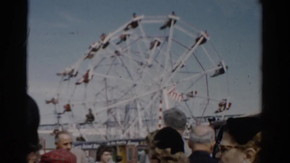 White Ferris wheel at a 1950s-era fair; several fairgoers' faces visible including a woman in glasses, Catskill area, New York, c. 1957.