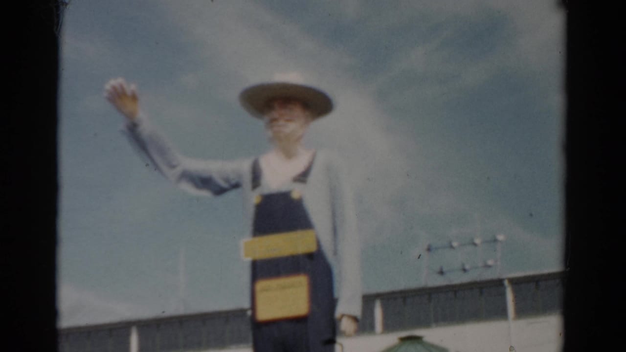 Farmer sculpture in overalls and wide-brimmed hat with arm raised; white fairground building roofline visible behind.