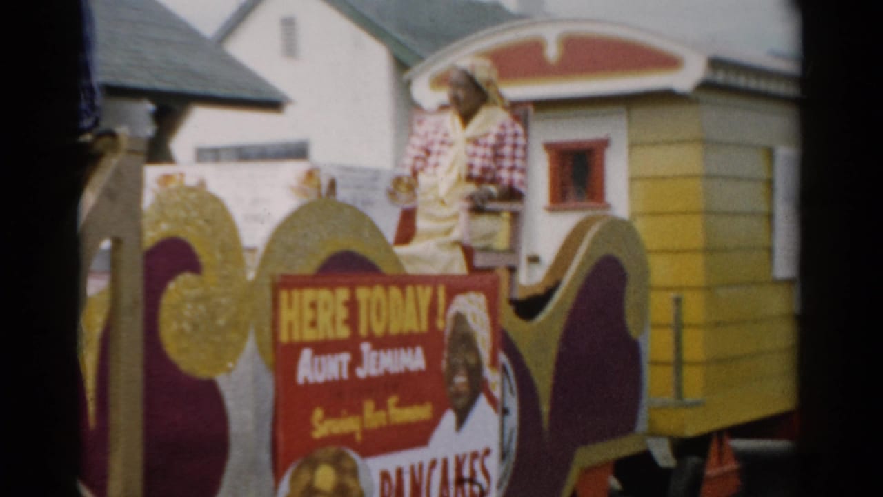 Close shot of the Aunt Jemima promotional parade float, c.1957, Catskill NY area, showing painted mascot panel and woman in checkered shirt above the 'Serving Her Famous Pancakes' signage.
