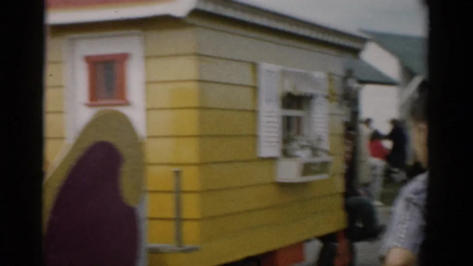 Close-up of the Aunt Jemima float's yellow-and-maroon house-shaped side wall with decorative red-trimmed windows, crowd of spectators visible in background, c.1957 upstate New York.