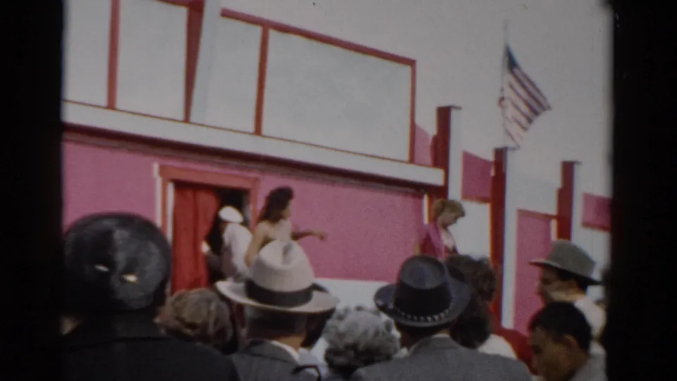 Red and white fair building facade at what appears to be the 1957 Catskill fair, American flag displayed, man in white hat and woman near entrance door in foreground.