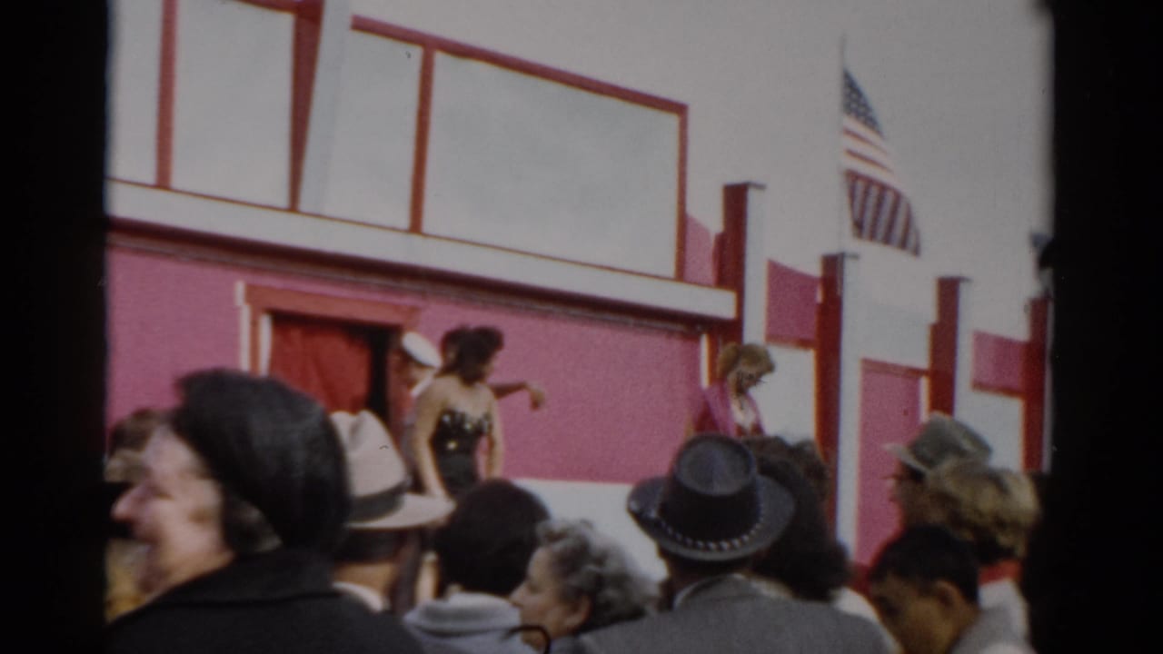 Crowd watches a costumed female performer on a pink-and-white fairground stage; American flag visible above.