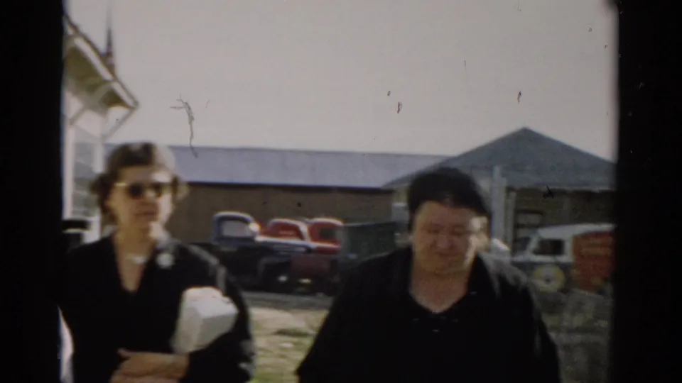 Two female visitors in 1950s dress walk toward camera at the Catskill Game Farm; red and cream vintage automobiles parked behind them, c. 1957.