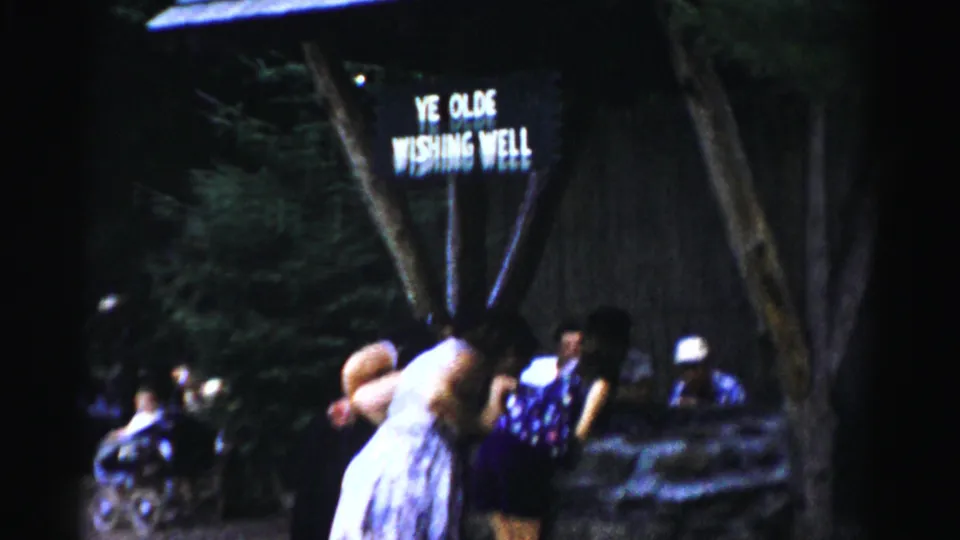 1957 Catskill home-movie frame with visitors in mid-century dress near the Ye Olde Wishing Well and a stroller visible at left.