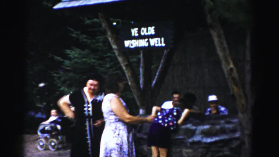 1957 Catskill frame showing visitors gathered at the Ye Olde Wishing Well, including a man in a dark vest and women in summer dresses.