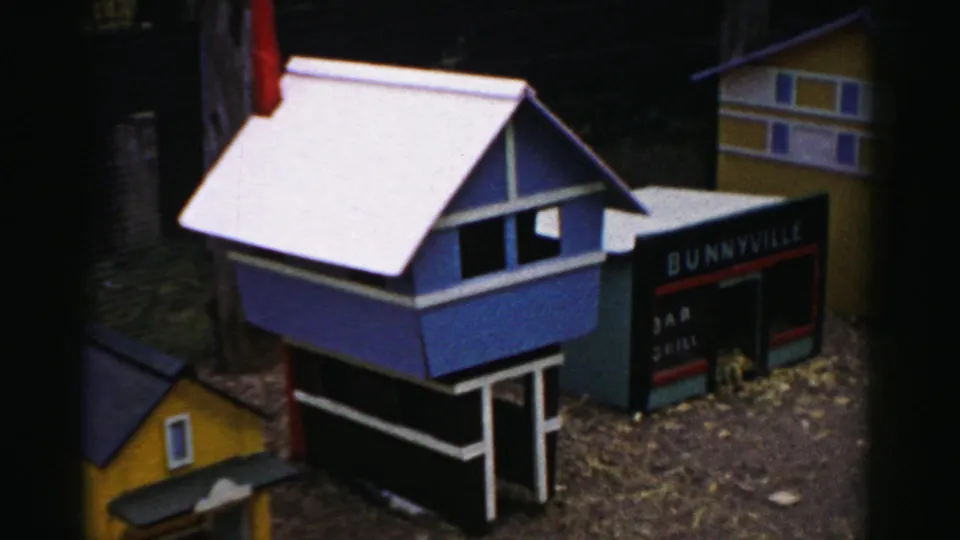 Blue miniature building with white roof beside a dark 'Bunnyville' sign showing partial additional text; yellow building at right; possibly a 1950s Catskill, New York tourist display.