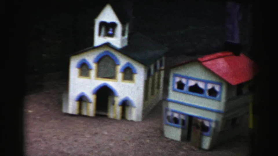 Hand-painted white miniature church with blue-trimmed Gothic arch windows and bell tower, alongside a red-roofed gray-walled structure; part of what appears to be a 1950s Catskill, New York tourist display.