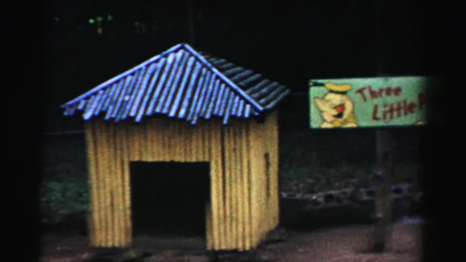 Yellow animal enclosure with partial Three Little Pigs sign at frame edge, likely at Catskill attraction, circa 1957, on 8mm color film.
