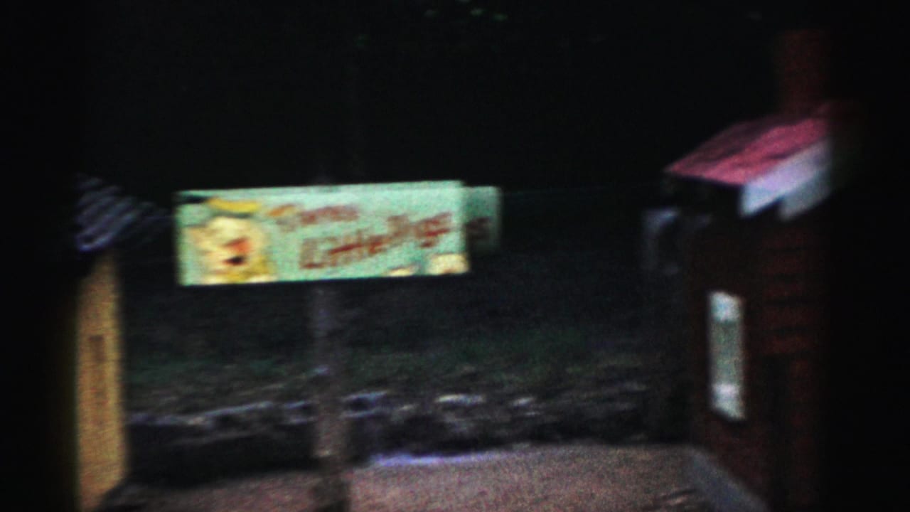 Nighttime 8mm shot of an illuminated sign with cartoon artwork at what may be a Catskill, New York roadside attraction, circa 1957