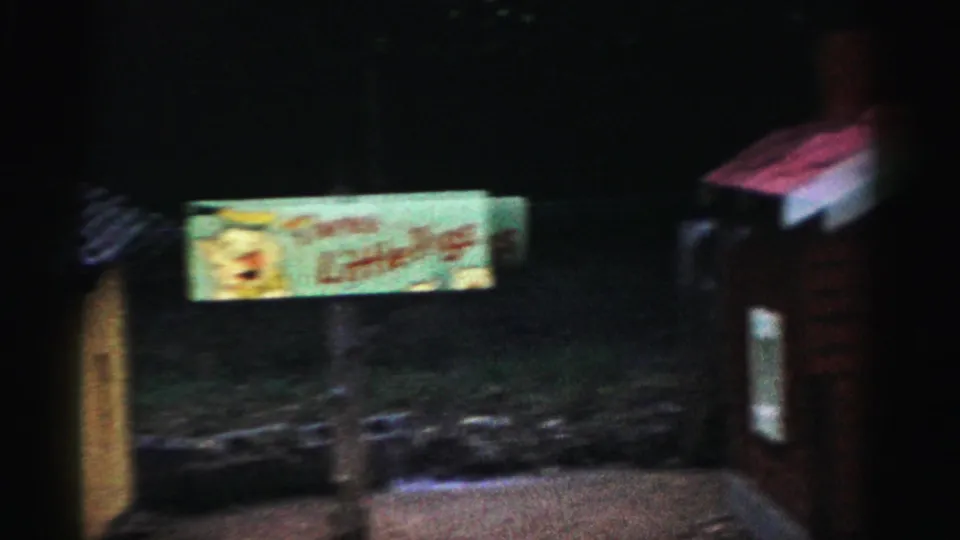 Nighttime 8mm shot of an illuminated sign with cartoon artwork at what may be a Catskill, New York roadside attraction, circa 1957