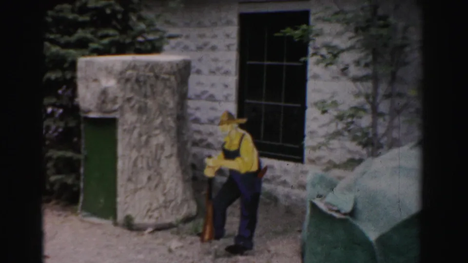 Man in yellow shirt and wide-brimmed hat at a zoo or animal park enclosure, Catskill area, New York, circa 1957, captured on 8mm home movie film.