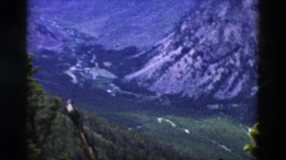 8mm frame circa 1958 of a rugged mountain range with snow remnants on upper slopes and pine trees, viewed from a high-elevation overlook.