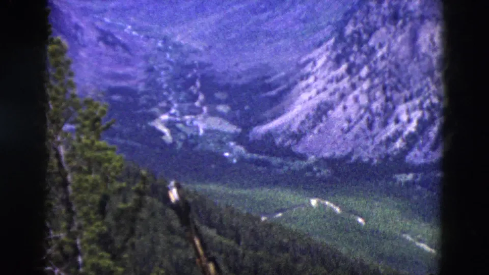 Closing pan frame showing full mountain vista with aged emulsion purple-blue tones and forested valley floor, Yellowstone area, Wyoming, 1958 8mm home movie.