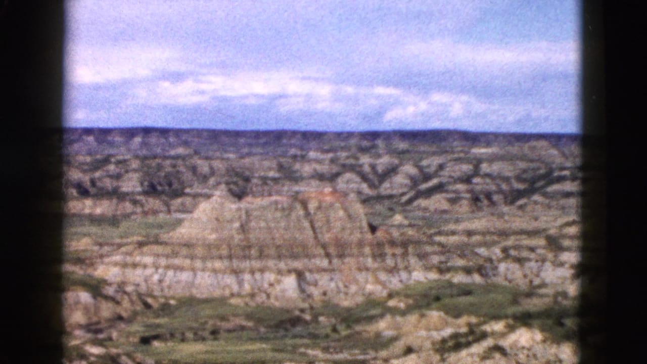 Eroded sedimentary rock formations in Wyoming filmed on 8mm circa 1958; visible strata bands and sparse valley vegetation stretch toward the horizon.