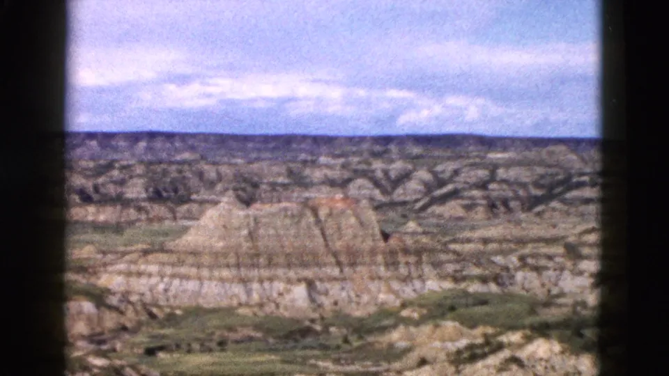 Eroded sedimentary rock formations in Wyoming filmed on 8mm circa 1958; visible strata bands and sparse valley vegetation stretch toward the horizon.