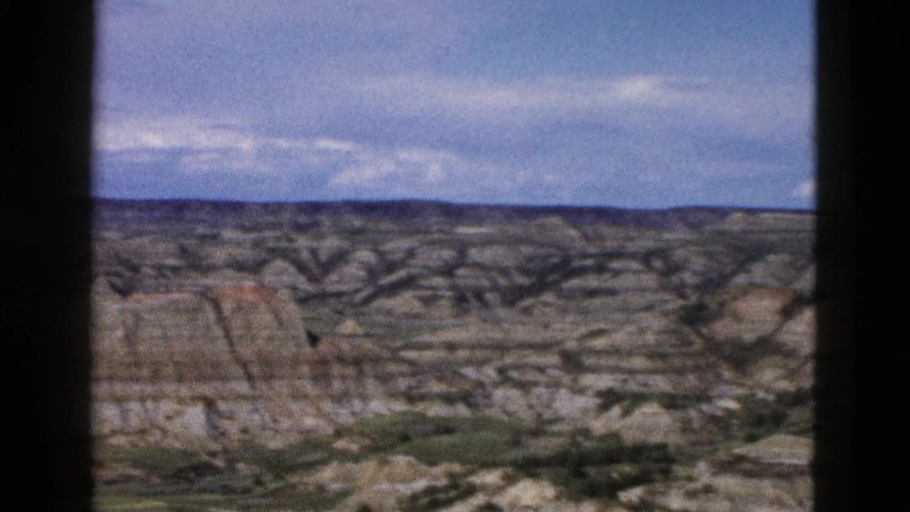 Layered eroded rock formations in the Wyoming landscape, 1958 8mm home movie; sedimentary strata and sparse low vegetation visible at base of formations.