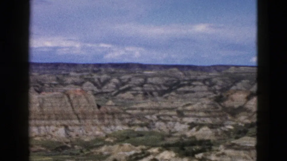 Layered eroded rock formations in the Wyoming landscape, 1958 8mm home movie; sedimentary strata and sparse low vegetation visible at base of formations.