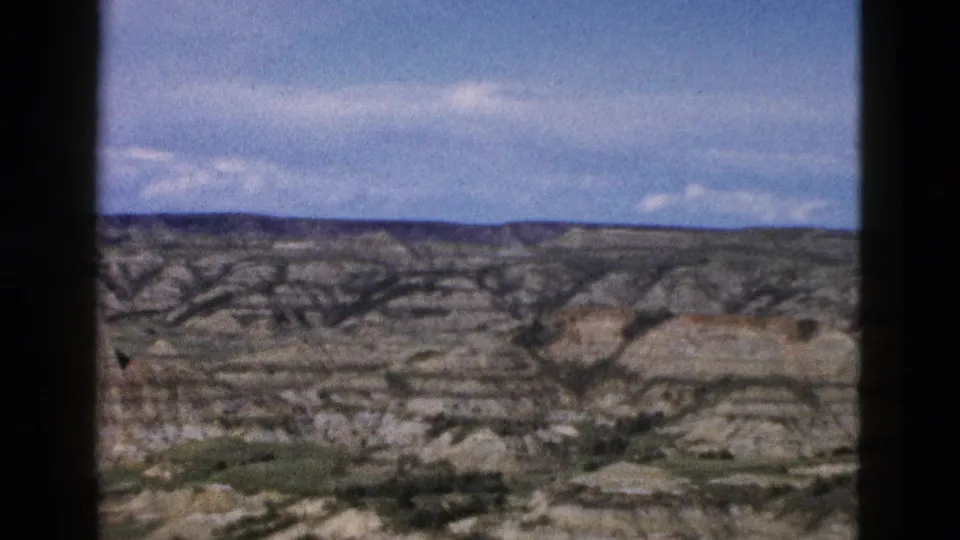 Wide-angle 8mm view of Wyoming eroded rock terrain circa 1958; formations recede toward the horizon under a broad sky with scattered cumulus.