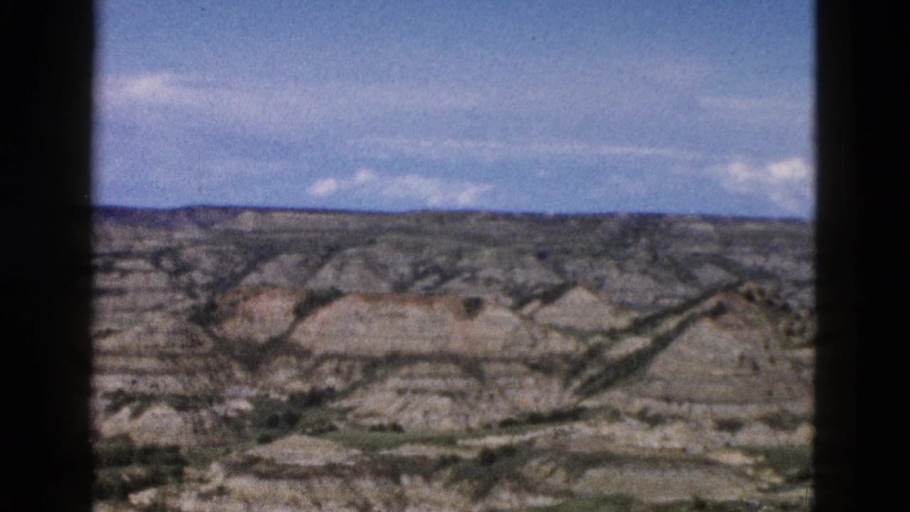 Eroded rock buttes and badlands terrain viewed through a car window, blue sky above, 8mm film