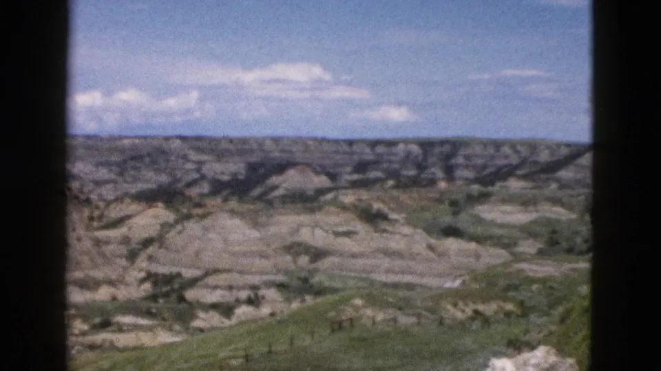Eroded rock formations and scrubland in Wyoming, ca. 1958, framed by dark car window edges, 8mm color film showing warm saturation