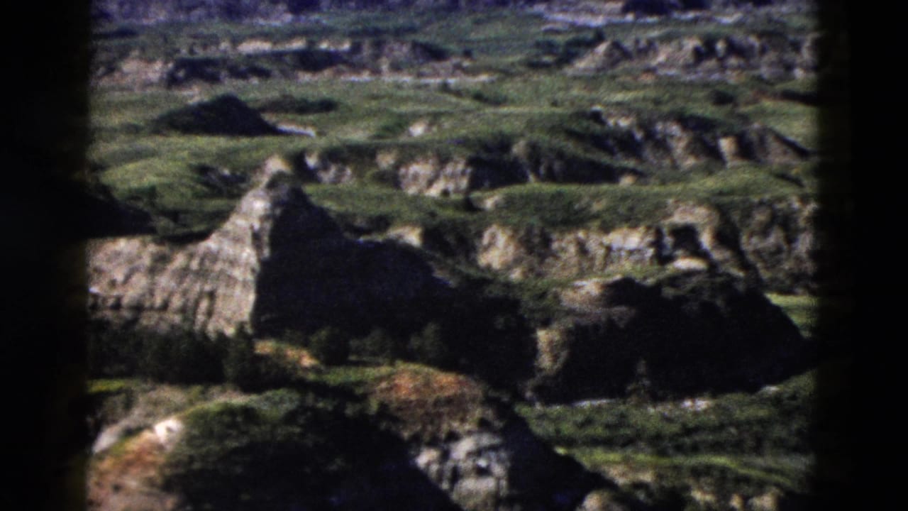 Eroded rock formations and jagged outcroppings with sparse green vegetation in a close-range landscape view, heavy dark borders at frame edges.