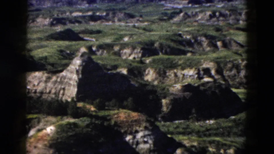 Close-range 8mm view of eroded canyon rock formations with patchy green vegetation, consistent with Wyoming badlands-type terrain circa 1958.