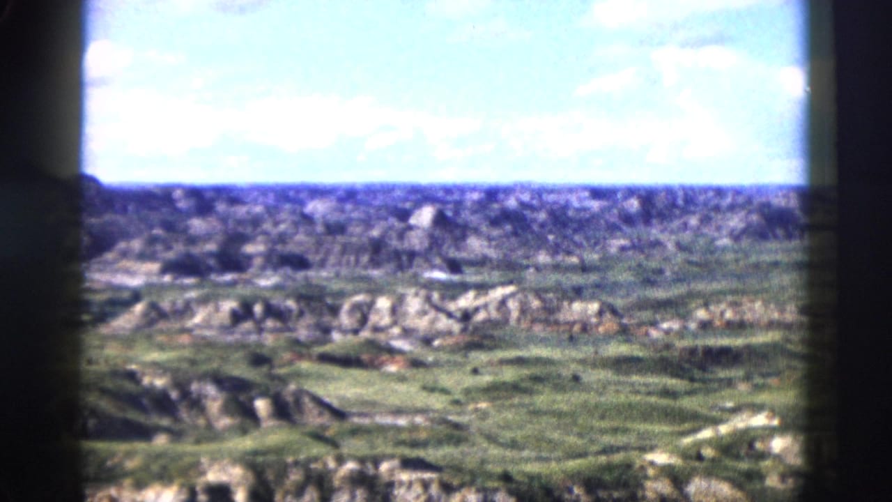 Panoramic 8mm shot of eroded rock formations and canyon terrain under blue sky with clouds, consistent with Wyoming landscape circa 1958.
