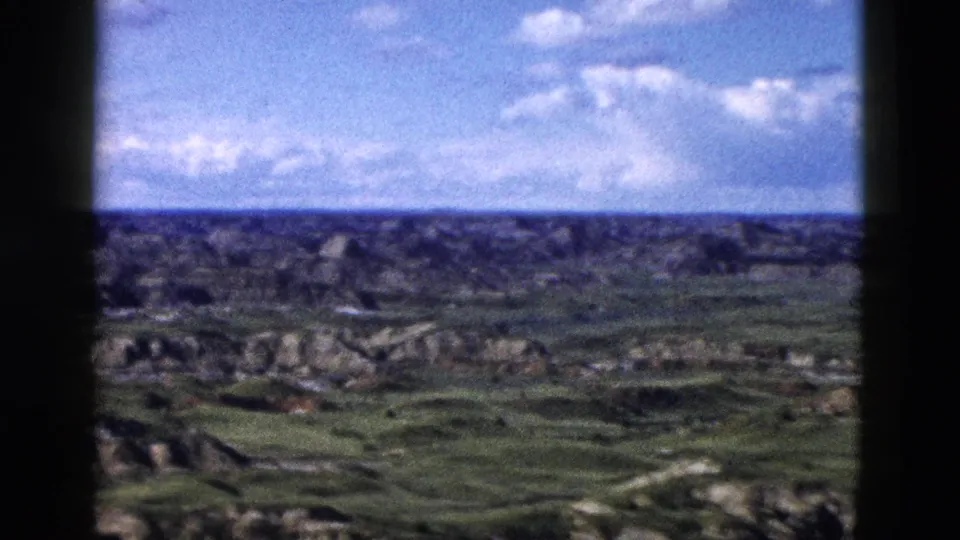 Wide 8mm panoramic shot of rugged Wyoming badlands-type terrain under an open blue sky with cumulus clouds, shot during a family road trip circa 1958.