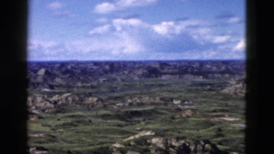 Continuing 8mm pan across rugged Wyoming canyon terrain under blue sky with cumulus clouds, consistent with late-1950s home-movie visitor footage.