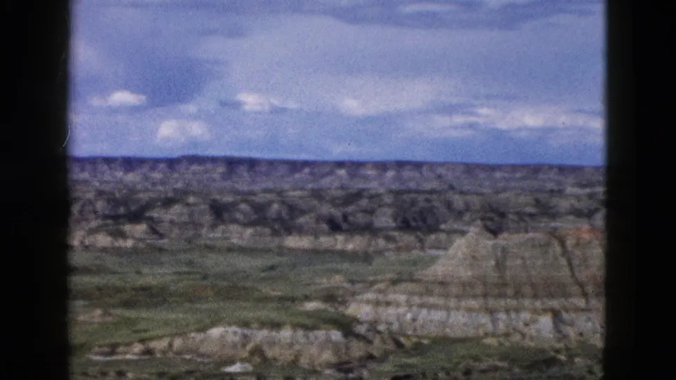 8mm frame showing a prominent butte amid eroded landscape and grassy valley, Yellowstone/Wyoming region, circa 1958.