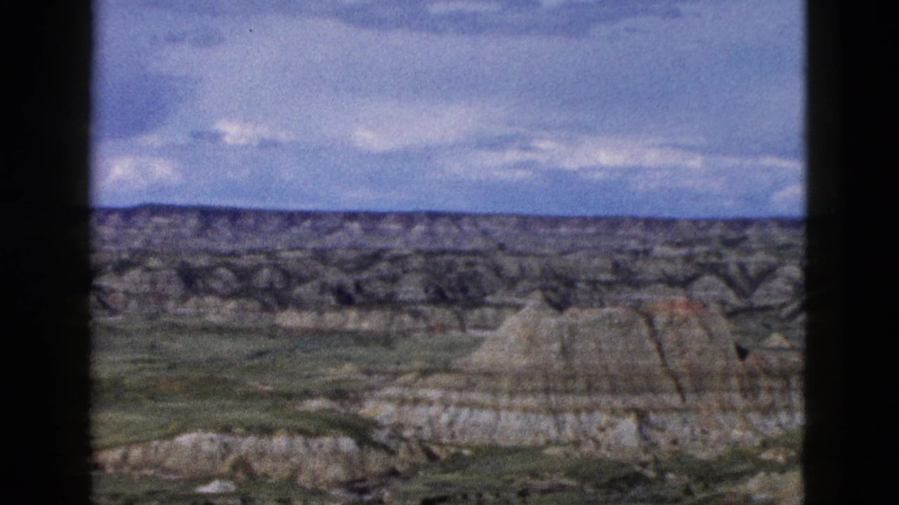 8mm home-movie frame c.1958 showing badlands-style eroded buttes with horizontal strata in Wyoming under a cloudy sky.