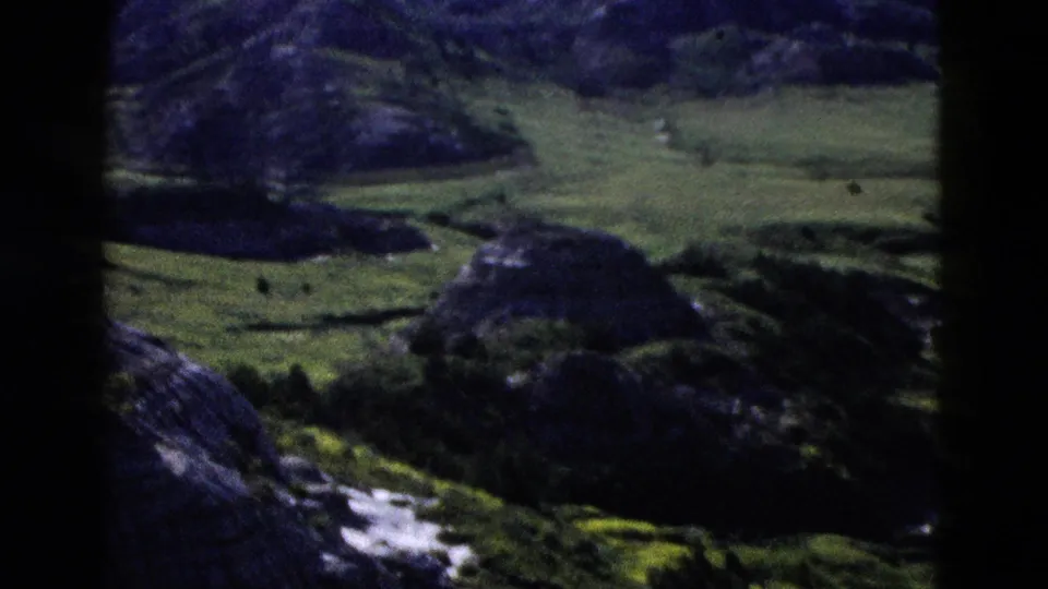 8mm home-movie frame c.1958 shot from an elevated overlook showing green valleys and dark rocky hills in Wyoming.